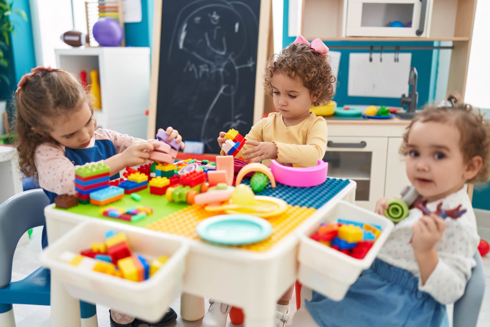 In Kids Summer Camp, Three young children playing with colorful building blocks and toys at a table in a vibrant classroom setting.