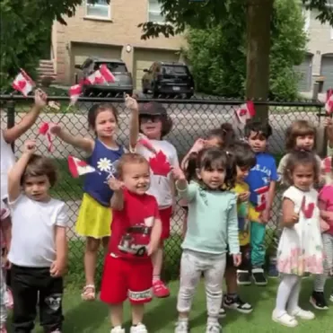 Group of children outdoors waving Canadian flags during a celebration.