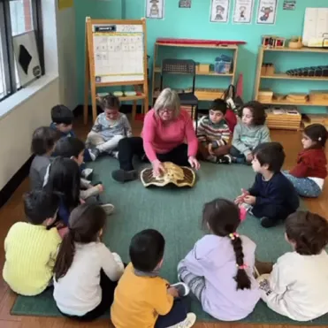 Teacher leading a group of children seated in a circle, showing a large turtle shell in a classroom activity.